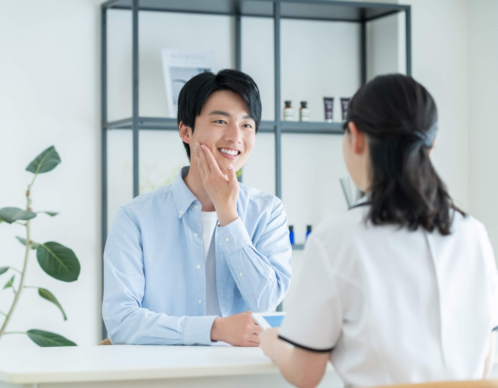 頬に手を当てて笑顔を見せる男性とスタッフがカウンセリングで対話している様子
