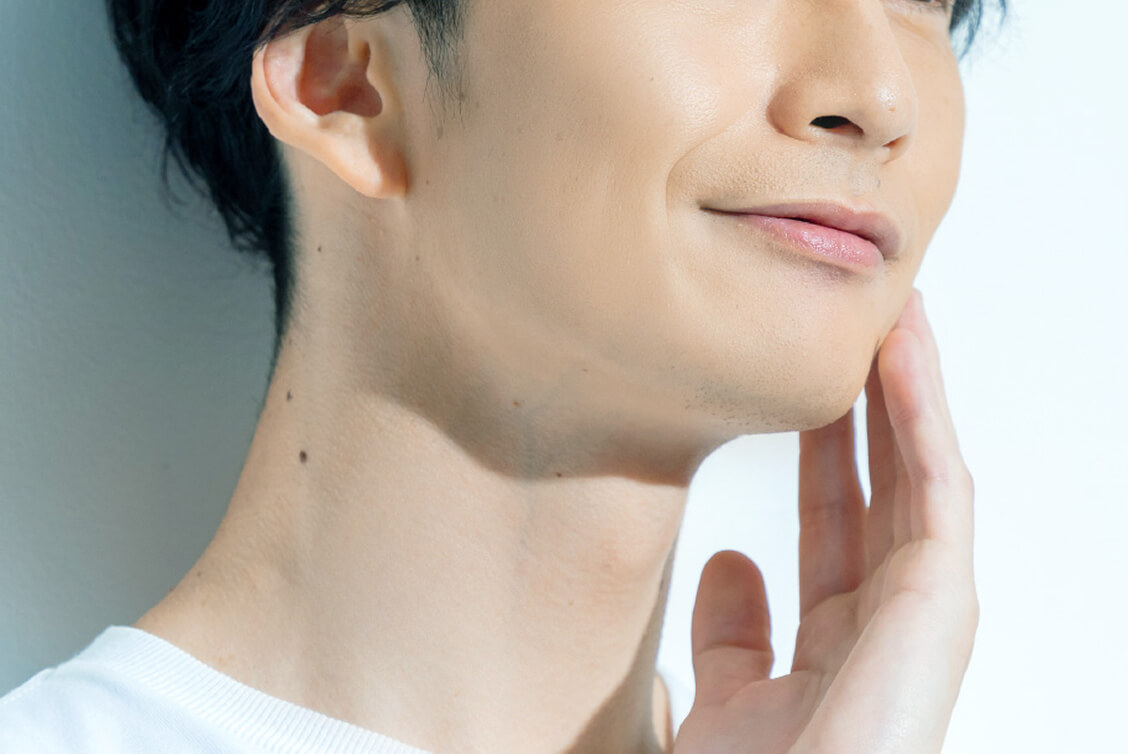 頬に手を当てて満足そうな表情を見せる男性。肌はスムーズで健康的な印象